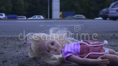 娃娃躺在马路附近，车水马龙. 许多汽车从后面来。